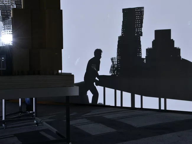 Perfromers push models of Frank Gehry's work around the exhibition according to a set of motions choreographed by artist Tino Sehgal.