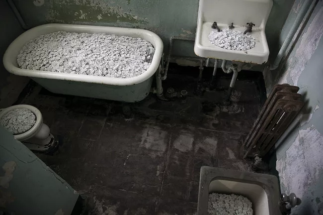 In some of the hospital cells, the artist has filled dilapidated toilets, sinks, and tubs with profusions of white porcelain flowers (<em>Blossom</em>). Like flourishing life poised to wash down the d