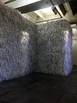 The exhibition includes a structure shaped like the perimeter of  Birkenau, enclosing a space that can’t be seen or entered. The wall is  covered with shredded paper, suggesting bits of logs and