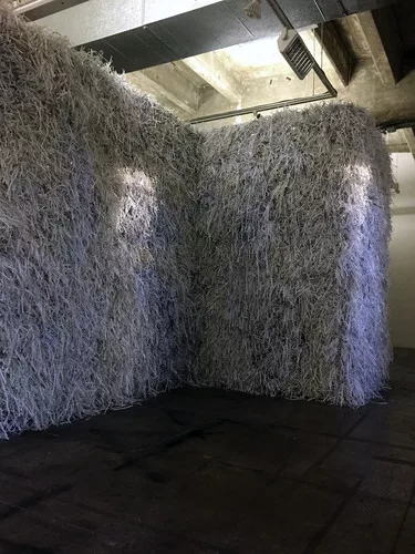 The exhibition includes a structure shaped like the perimeter of  Birkenau, enclosing a space that can’t be seen or entered. The wall is  covered with shredded paper, suggesting bits of logs and