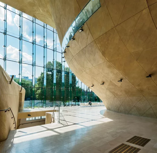 The boxy museum, which is clad in angled fritted-glass panels separated by strips of perforated copper, conceals a cavernous entrance hall with curving concrete walls and a travertine floor.