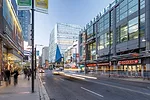 The building's distinctive form and the blue shard of the entrance canopy visually mark the gateway to Ryerson University amid the retail patchwork of the busy downtown street.