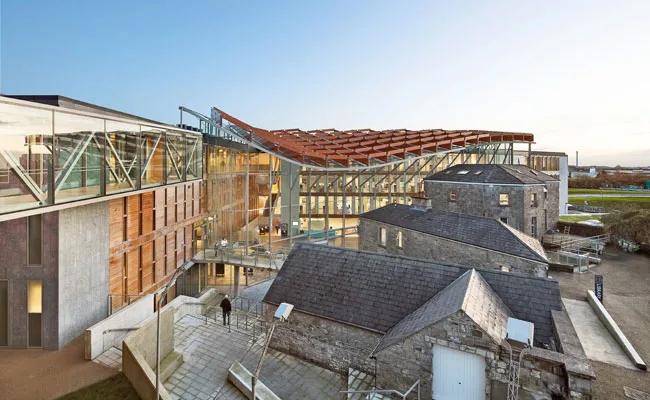 To reach the library, visitors walk past a set of early-20th-century buildings and remnants of a 19th-century prison, then cross an exposed concrete bridge to a second-floor entrance.