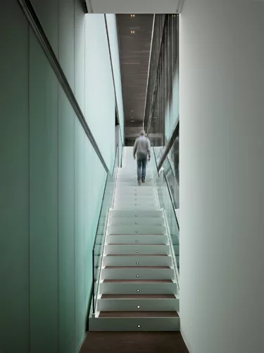 The major stair rises across the glazed court elevation, while a translucent and mirrored-glass wall separates the stair from the galleries.
