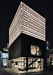Illuminated panels of punched anodized aluminum transform the shop&rsquo;s hollow third layer into a lantern by night.