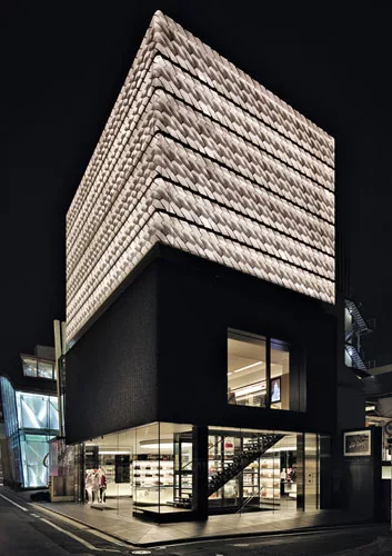 Illuminated panels of punched anodized aluminum transform the shop&rsquo;s hollow third layer into a lantern by night.