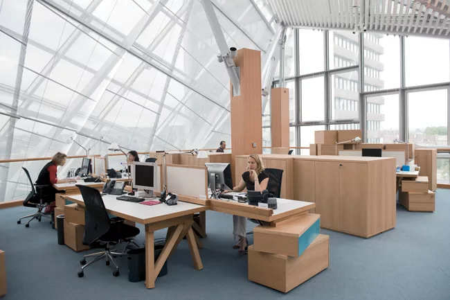 Employees sitting at workstations designed by Frank Gehry are protected from the sun&rsquo;s glare by a sophisticated system of saillike shades, controlled by daylight sensors. Artemide Tolomeo desk l