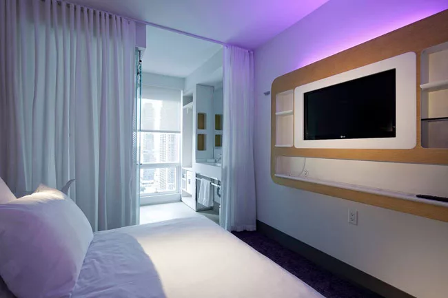 For the compact rooms, linear fluorescent lamps hidden behind a TV-and-storage console provide ambient light. One is wrapped in a purple gel sleeve.