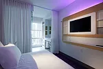 For the compact rooms, linear fluorescent lamps hidden behind a TV-and-storage console provide ambient light. One is wrapped in a purple gel sleeve.