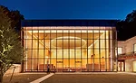 Framed by landscaped grounds and the evening sky, the temple&rsquo;s north-facing window wall reveals a soaring sanctuary dramatically illuminated by a luminous mesh circle of light and a floating cei