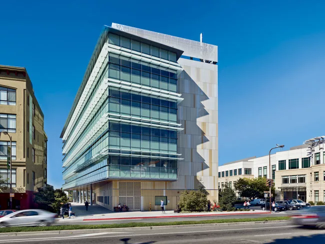 The offices are housed in a wedge that protrudes from the building's south side and wraps a corner. On the exterior of this glazed volume, a series of laminated glass shades directs and diffuses dayli