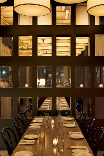 The private dining area (left) features a wall grid inset with a playful mix of mirrors and windows. These either reflect the barrel shades within the room or provide glimpses of the ceiling grid&mdas