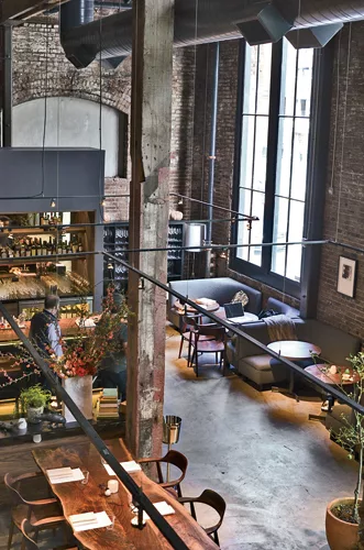 An exposed white kitchen spills into Saison’s dining area (slide 2). To minimize the room’s height—which peaks at 30 feet—interior designer Jiun Ho suspended steel frames from