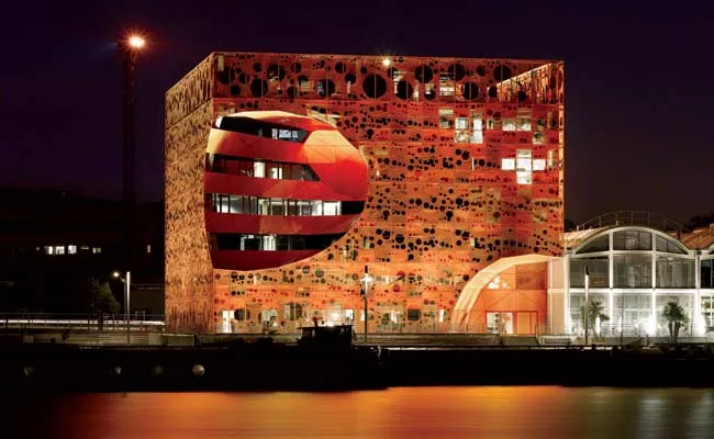 Located in a former dockland, the new commercial building is clad in an aluminum scrim whose pattern was inspired by the movement of water.