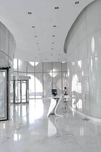 In the lobby, the architects designed the powder-coated aluminum reception desk to echo the curve of the walls and blend in with the luminescent white marble floors.
