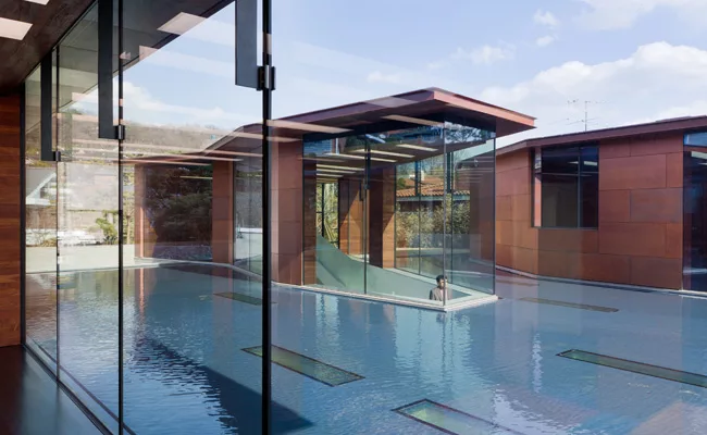 A trio of copper-clad pavilions rise above the plane of a reflecting pool, while linear skylights set in the pool bring daylight to galleries below.