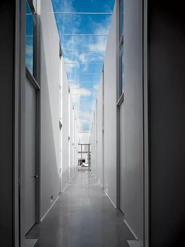 The soaring, double-loaded corridor is animated by a crystal-clear linear skylight and shadows cast from above.