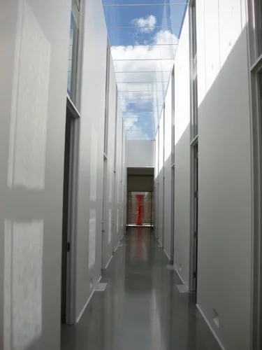 A red painted steel sculpture by Nigel Hall is visible at the end of the long, skylit corridor.