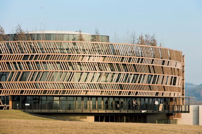 Behind the larch wood screen, the glass is tinted gray so that the screen is prominent. The lowest floor follows the drop in grade where the architects inserted a glass-enclosed picnic area for childr