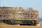 Behind the larch wood screen, the glass is tinted gray so that the screen is prominent. The lowest floor follows the drop in grade where the architects inserted a glass-enclosed picnic area for childr