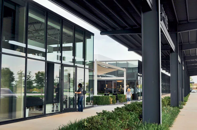 Steel canopies shade customers as they walk between the stores. Landscaping extends to these interstitial spaces.