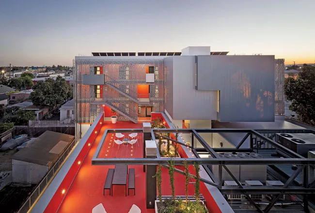 An outdoor lounge, with a vermilion elastomeric surface, connects the old and new buildings. The addition's aluminum sunscreen has a punched pattern abstracted from the main entrance's 1920s bas-relie