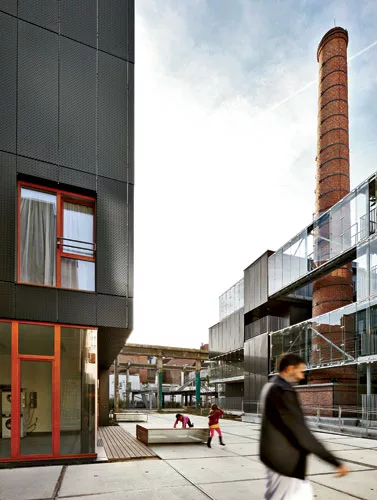 Children play on the Grande Cour of the former soap factory turned public-housing project, where an old chimney rises among new buildings and the remains of a 1950s warehouse are now a bilevel playgro