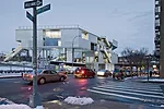 The building's porosity is apparent when it is viewed from the southwest. The aluminum used for the cladding appears at the building's base and on its balustrades with an abstracted laser-cut pattern.