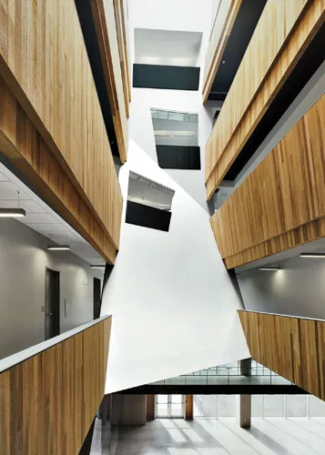 The two wedge-shaped atriums of the pharmaceutical building are clad in  cedar, and skewed openings in a canted white gypsum-board wall along the south end of the east atrium reveal glimpses of the pe