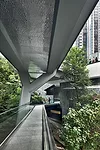 A double-level footbridge extends on the east from the roof garden of the new main pavilion and the plaza of the lobby level below. The walkway, marked by concrete Y-shaped supports, glazed ceramic ti