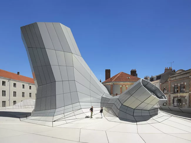 The digitally computed, faceted form with irregular angles is covered by a rainscreen of aluminum panels, and below them, precast concrete panels. Brendan MacFarland (left) talks to photographer Rolan