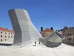 The digitally computed, faceted form with irregular angles is covered by a rainscreen of aluminum panels, and below them, precast concrete panels. Brendan MacFarland (left) talks to photographer Rolan