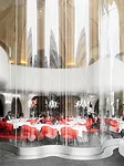 Tailored to the existing building, the undulating glass facade wends its way around the stone columns and soars to the curved ceiling. A steel band embedded in the new floor secures the wall's base.