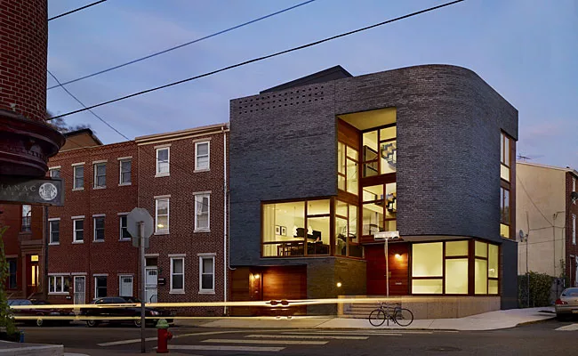 The facade, with a bullnose corner, presents a striking contrast of masses and voids: Gray brick and sapele wood cladding are punctuated by glass expanses with mahogany frames that seem to defy struct