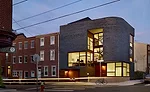 The facade, with a bullnose corner, presents a striking contrast of masses and voids: Gray brick and sapele wood cladding are punctuated by glass expanses with mahogany frames that seem to defy struct