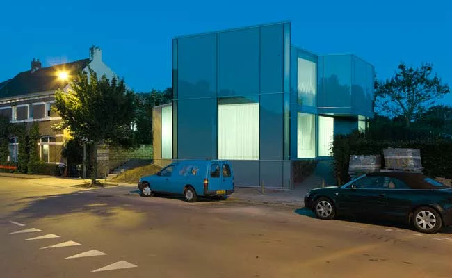  The two-story house is sheathed in translucent, opaque, and transparent glass, with curtains added for privacy and glare reduction.