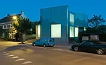  The two-story house is sheathed in translucent, opaque, and transparent glass, with curtains added for privacy and glare reduction.