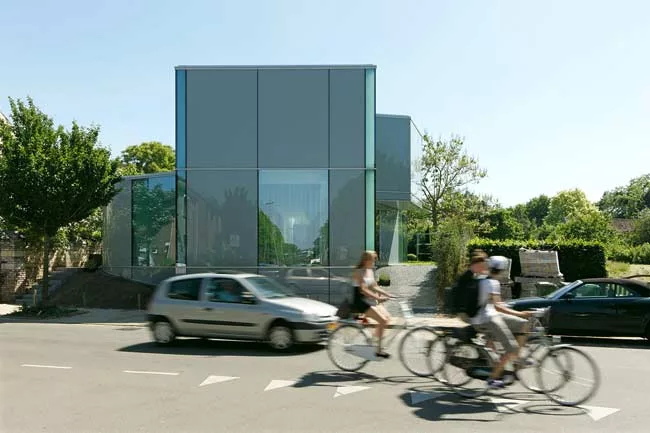 The two-story house is sheathed in translucent, opaque, and transparent glass, with curtains added for privacy and glare reduction.