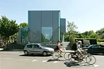 The two-story house is sheathed in translucent, opaque, and transparent glass, with curtains added for privacy and glare reduction.