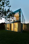 The two-story house is sheathed in translucent, opaque, and transparent glass, with curtains added for privacy and glare reduction.
