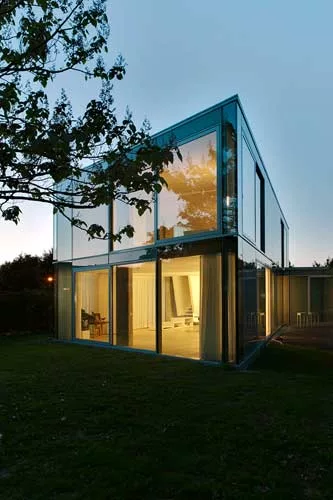 The two-story house is sheathed in translucent, opaque, and transparent glass, with curtains added for privacy and glare reduction.