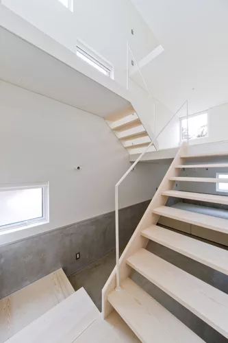 A staircase with treads of unpainted laurel wood leads from the ground level's concrete floor to the mezzanine levels above.