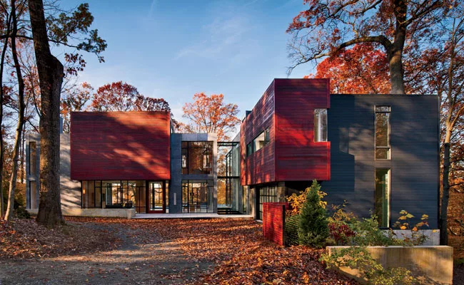 Architect Robert Gurney preserved trees by siting the house around an existing driveway. A glass bridge crosses a reflecting pool and connects the two volumes.