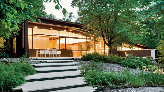 At the rear of the house, a glazed facade opens to a deck, which leads to a stepped garden and pool house.