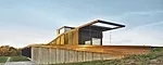 Set into a gentle grassy slope, the house has a copper roof and concrete-fiber rainscreen walls with black aluminum fins. 