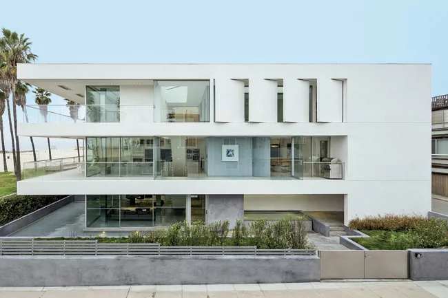 The minimalist three-story house is punctuated by movable walls on the top floor and deep overhangs.