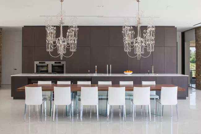 The dining table appears to float, thanks to its base of angled glass fins. The architects installed two chandeliers because “one is a focal point, but two create a line,” says Kelly.