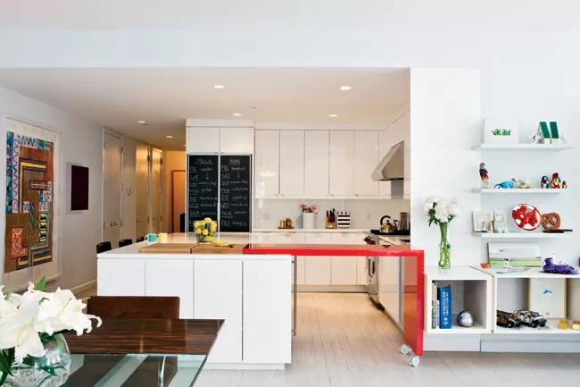 Glossy white kitchen cabinets serve as a neutral backdrop for the client’s collection of vintage furniture, such as the early 1970s-era dining table by Vladimir Kagan.