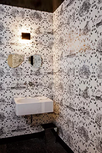 The powder room features traditional materials with a twist. The black-and-white wall covering is a slightly risqué variation on toile, the sink was originally designed for the German school syst