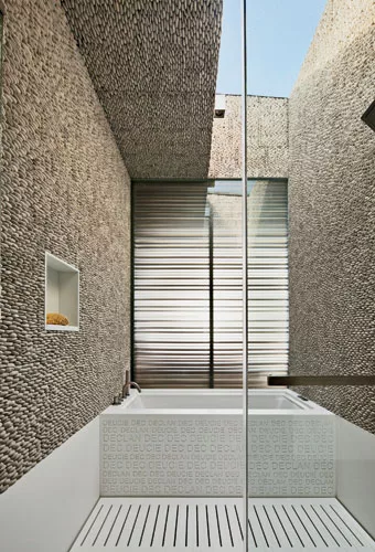 Pebble wall tiles in a child’s bath emphasize the interplay of light and shadow. They envelop a custom solid-surfacing tub surround carved with nicknames, as well as a slotted solid-surfacing dr